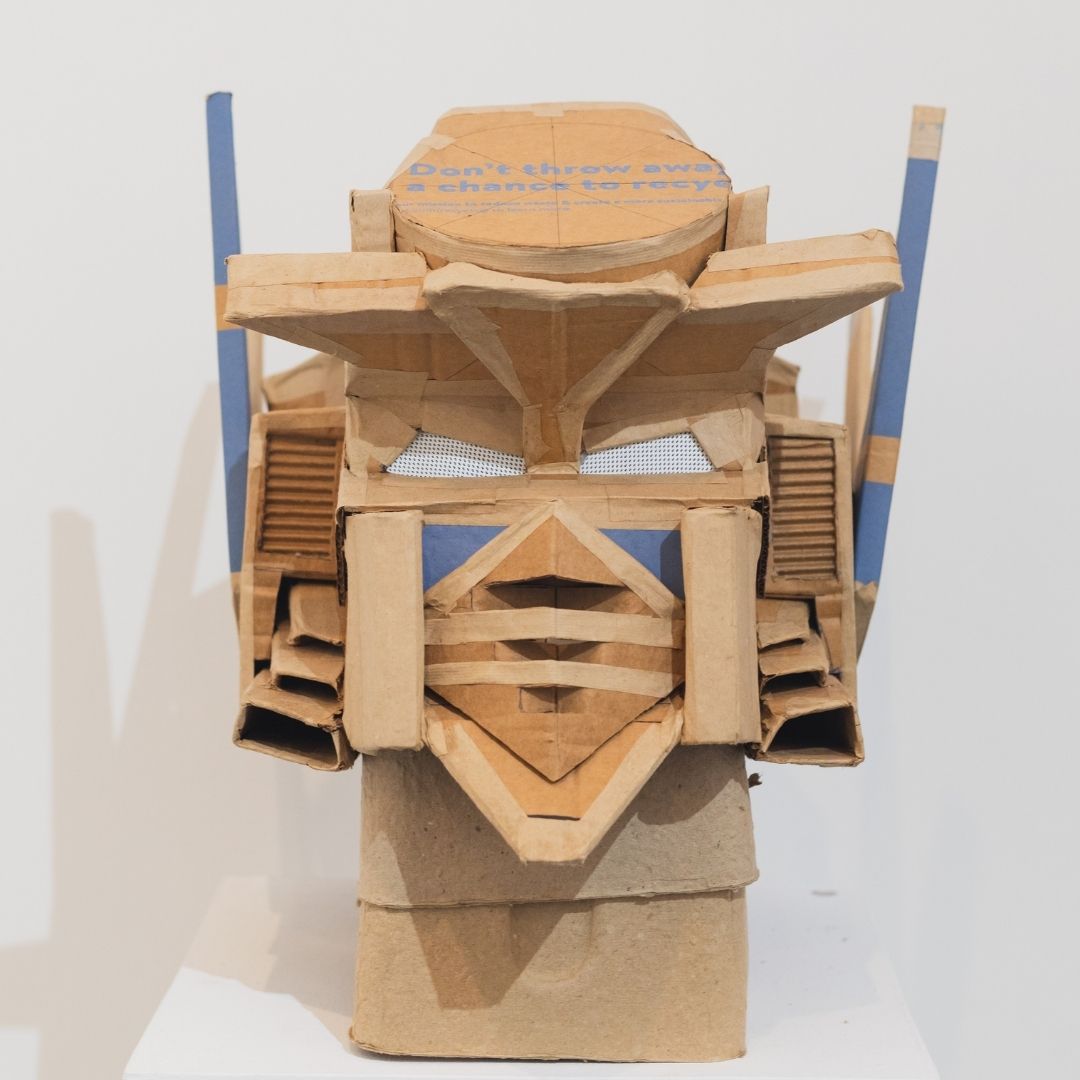 A sculpture of a robot mask made from recycled cardboard. 